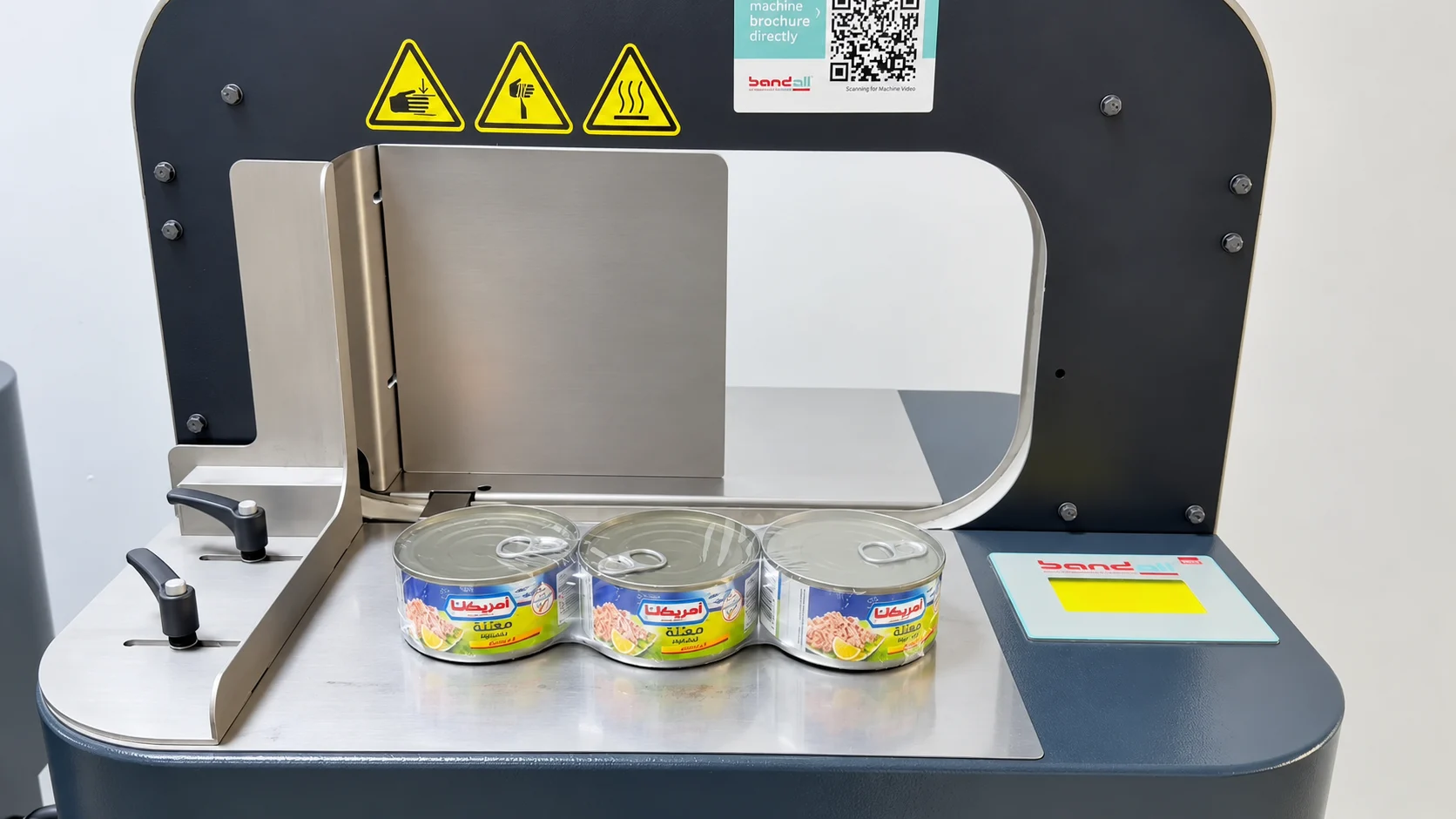 Three tuna cans wrapped in shrink film on the banding machine table, before banding